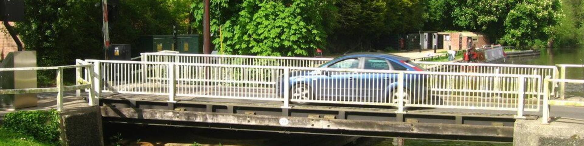 A narrow canal with a pedestrian bridge and a car crossing.