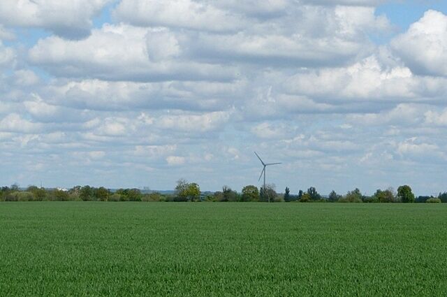 A green field with a wind turbine in the distance and a cloudy sky.
