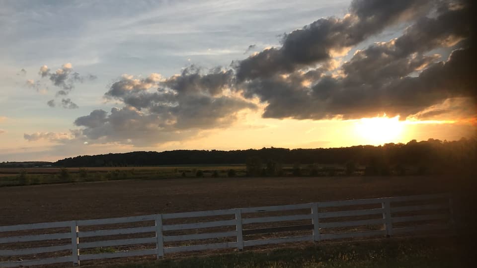 A sunset over a rural landscape with a white fence in the foreground.