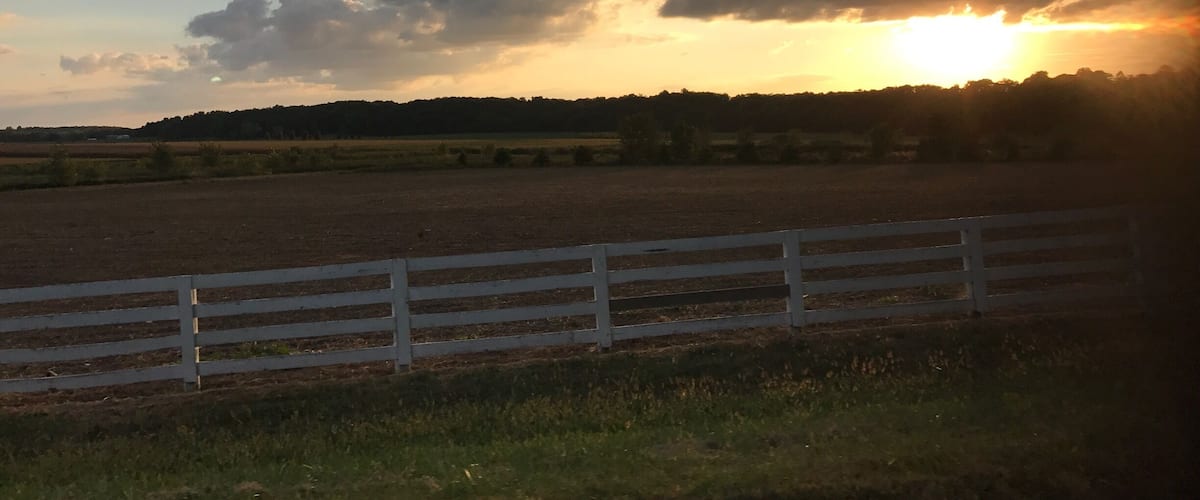 A sunset over a rural landscape with a white fence in the foreground.