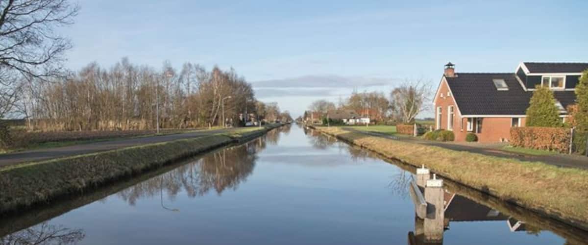 A calm canal with houses on one side and trees on the other.