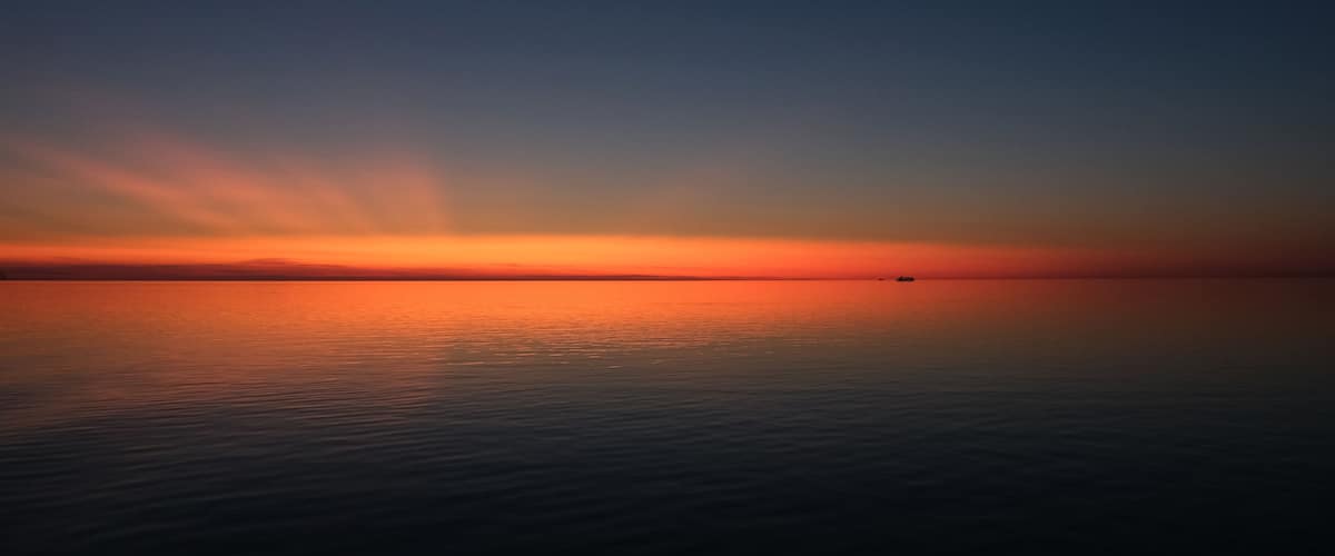 A calm sea at sunset with a gradient sky from orange to blue.