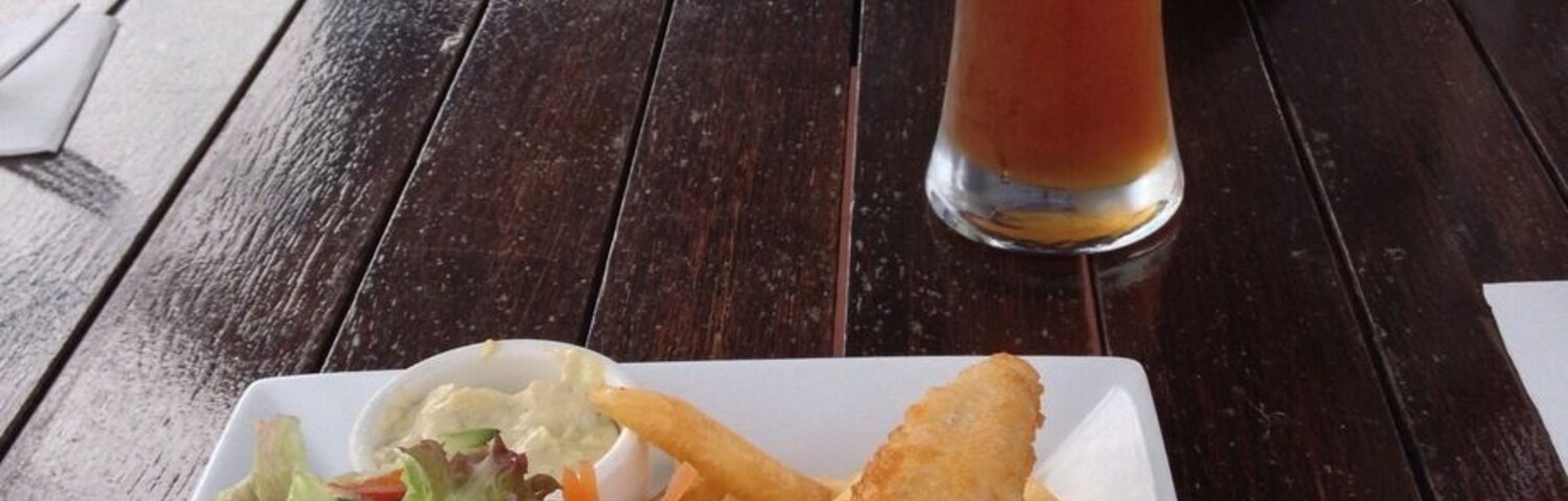 A meal of fish and chips with a side salad and a glass of beer on a wooden table.