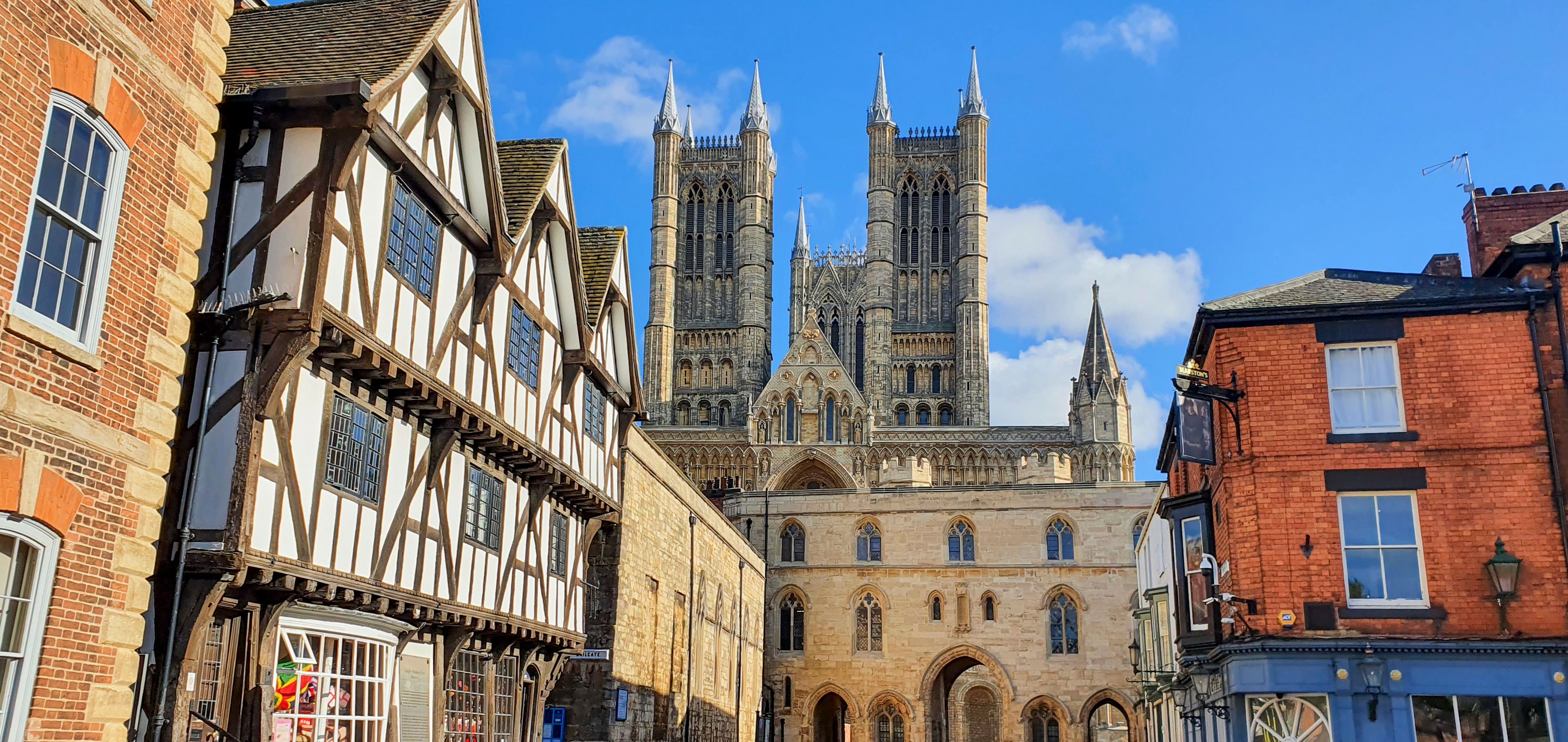 A historic street with Tudor-style half-timbered houses and a prominent Gothic cathedral in the background.