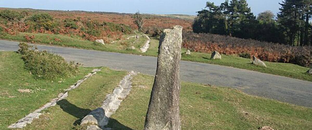 A stone monument in a grassy field with a road in the background.