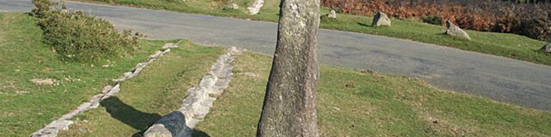 A stone monument in a grassy field with a road in the background.