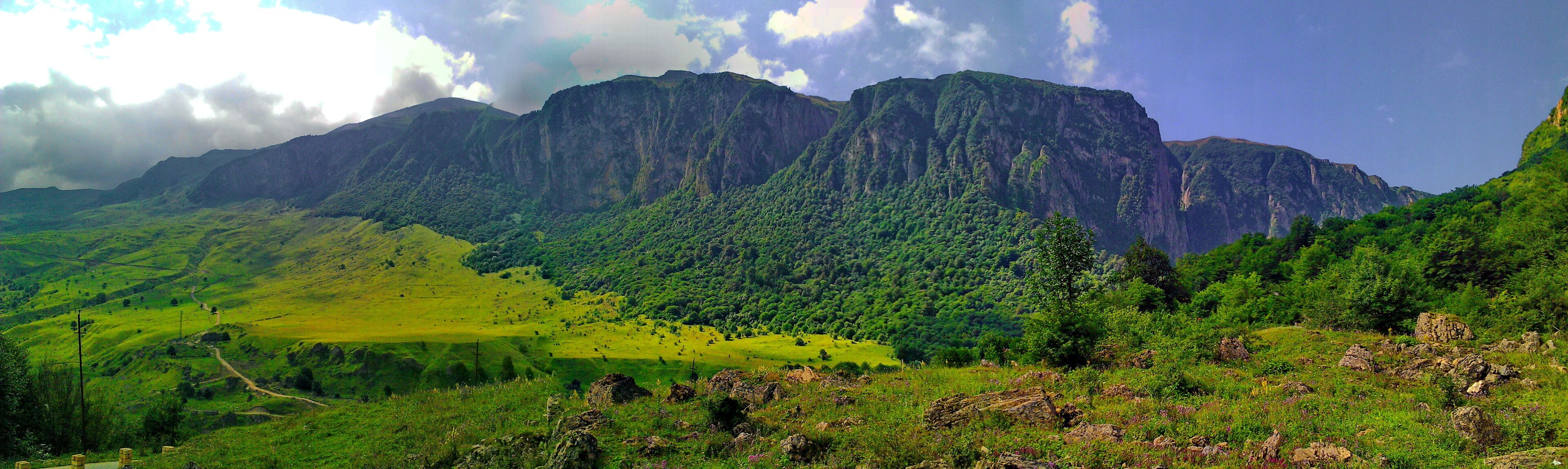 A mountainous landscape with lush green hills and a prominent rocky mountain range in the background.