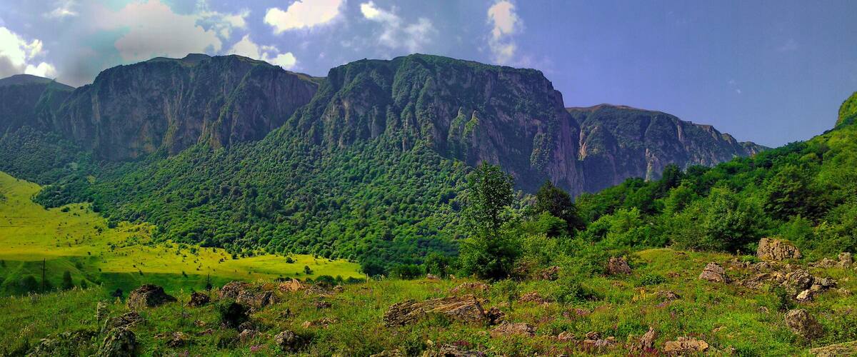 A mountainous landscape with lush green hills and a prominent rocky mountain range in the background.
