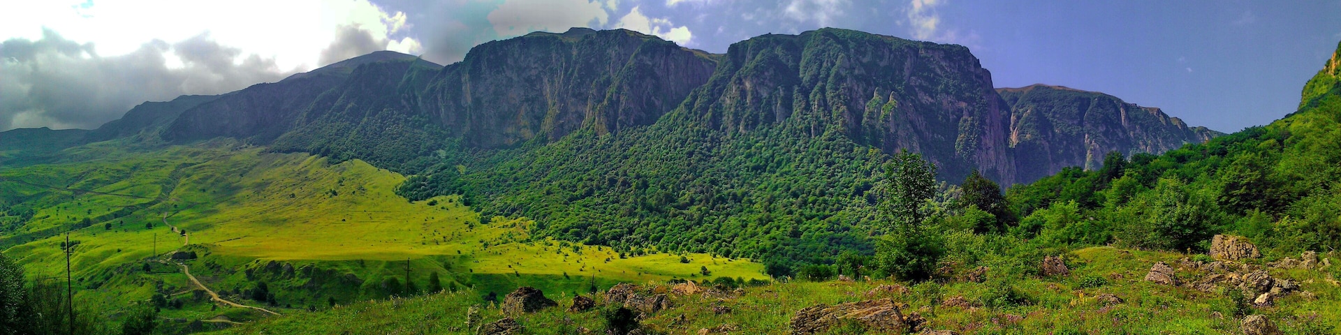 A mountainous landscape with lush green hills and a prominent rocky mountain range in the background.