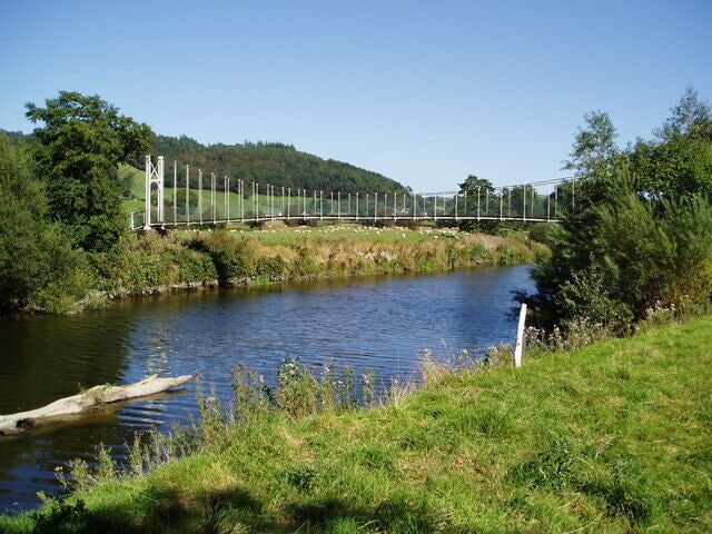 A river with a bridge, greenery, and a clear sky.