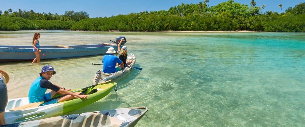 People in kayaks on a clear turquoise sea with a forested island in the background.
