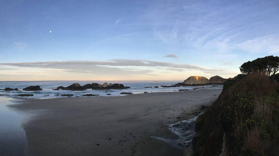 A coastal landscape with a sandy beach, rocky outcrops, and a clear sky.