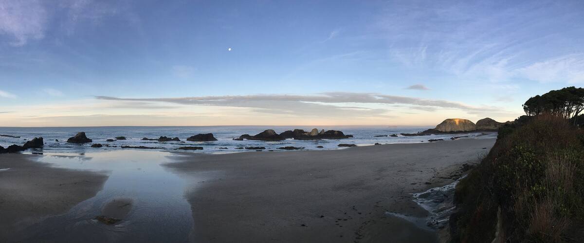 A coastal landscape with a sandy beach, rocky outcrops, and a clear sky.