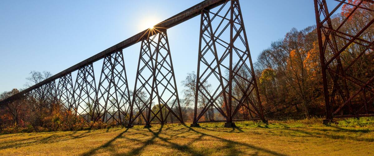 A large steel bridge with a sun shining through its structure.