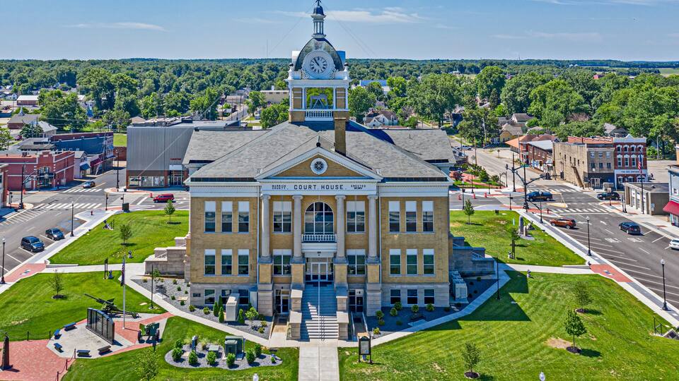 A courthouse with a clock tower, surrounded by a well-maintained lawn and a busy street.