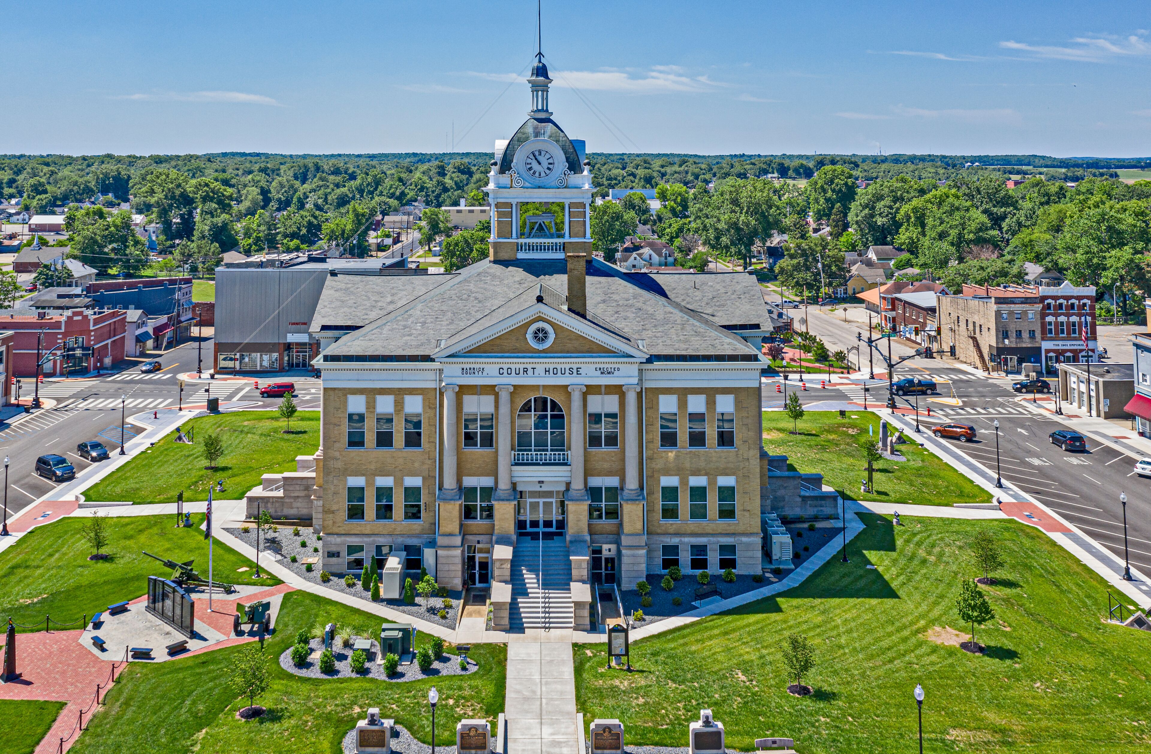 A courthouse with a clock tower, surrounded by a well-maintained lawn and a busy street.
