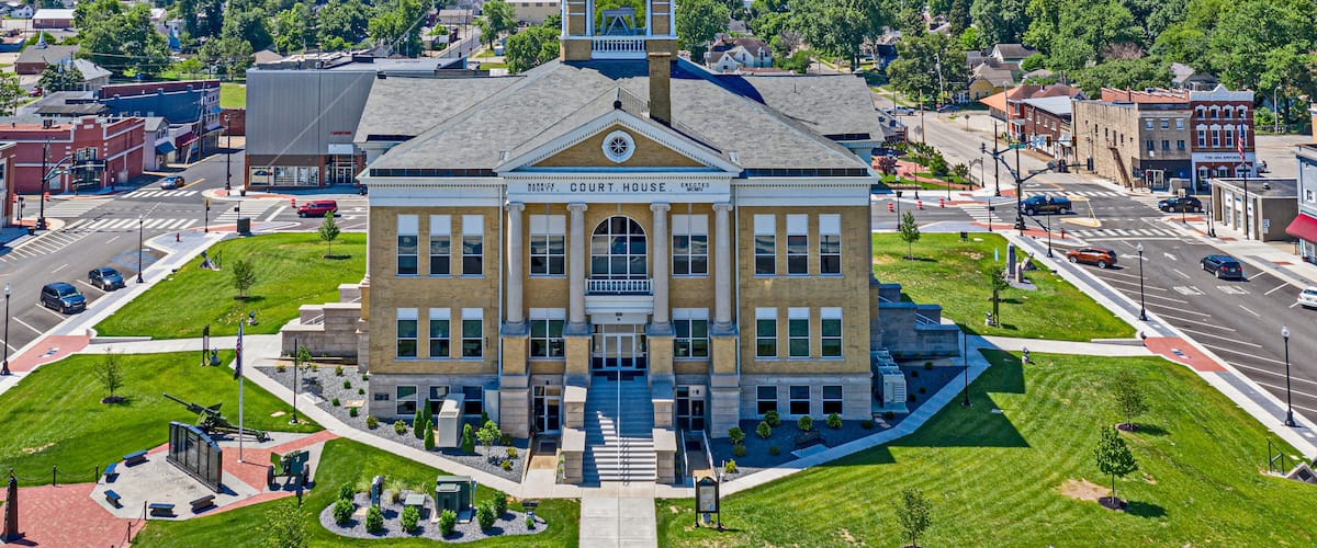 A courthouse with a clock tower, surrounded by a well-maintained lawn and a busy street.