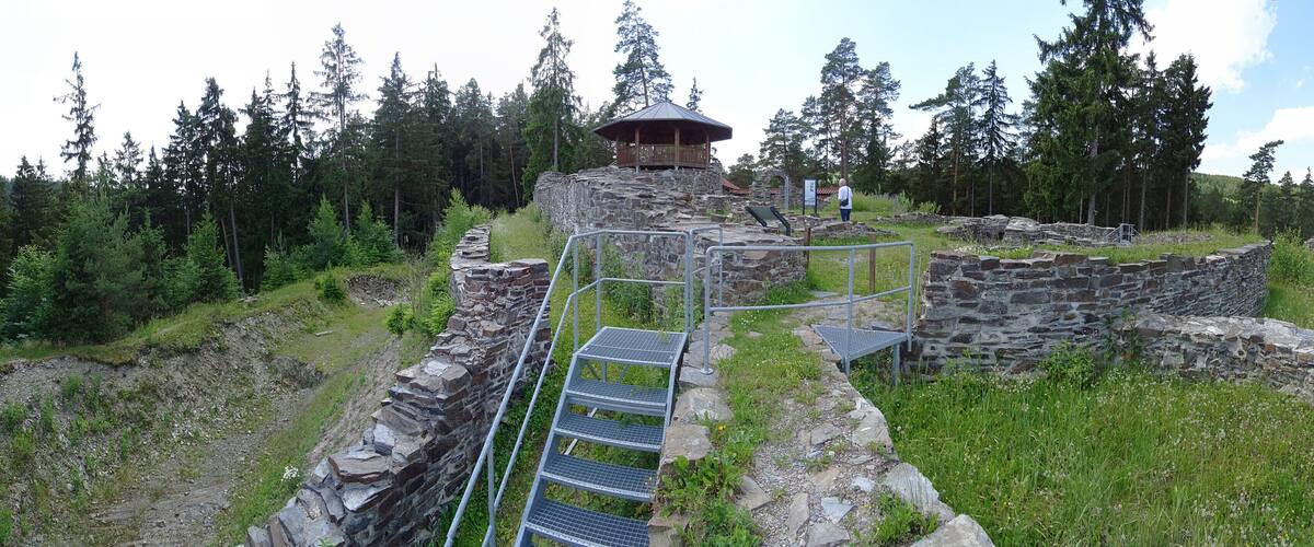 A stone ruin with a wooden viewing platform and metal stairs leading up to it, surrounded by a forest.