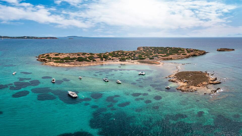 The little island Ydrousa off the coast of Voula, south Athens, Greece, with turquoise sea and a beautiful beach next to moored boats