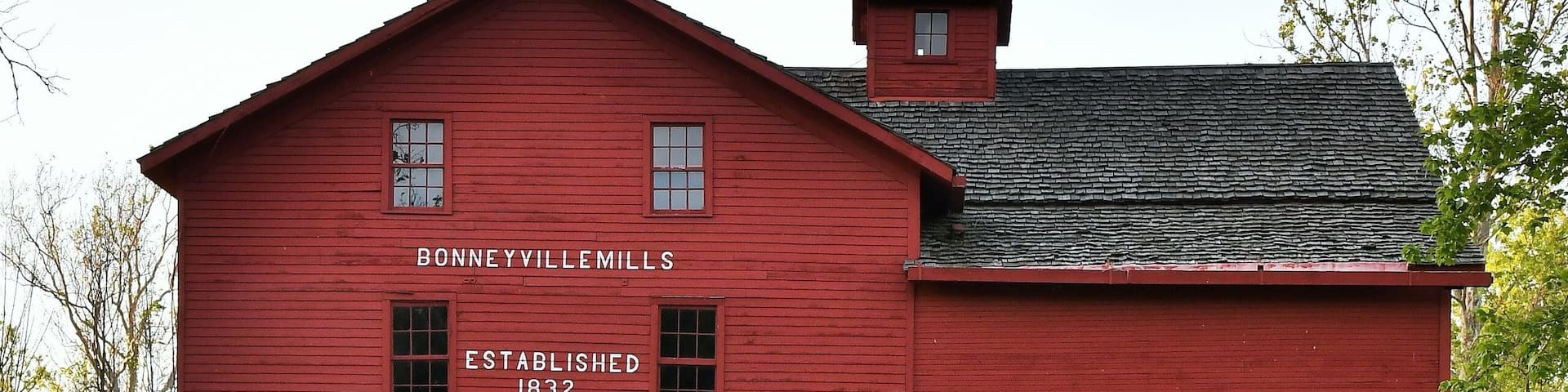 Daytime photo of the red barn mill at Bonneyville Mills in Bristol, Indiana with a calm pond and reflection in the foreground