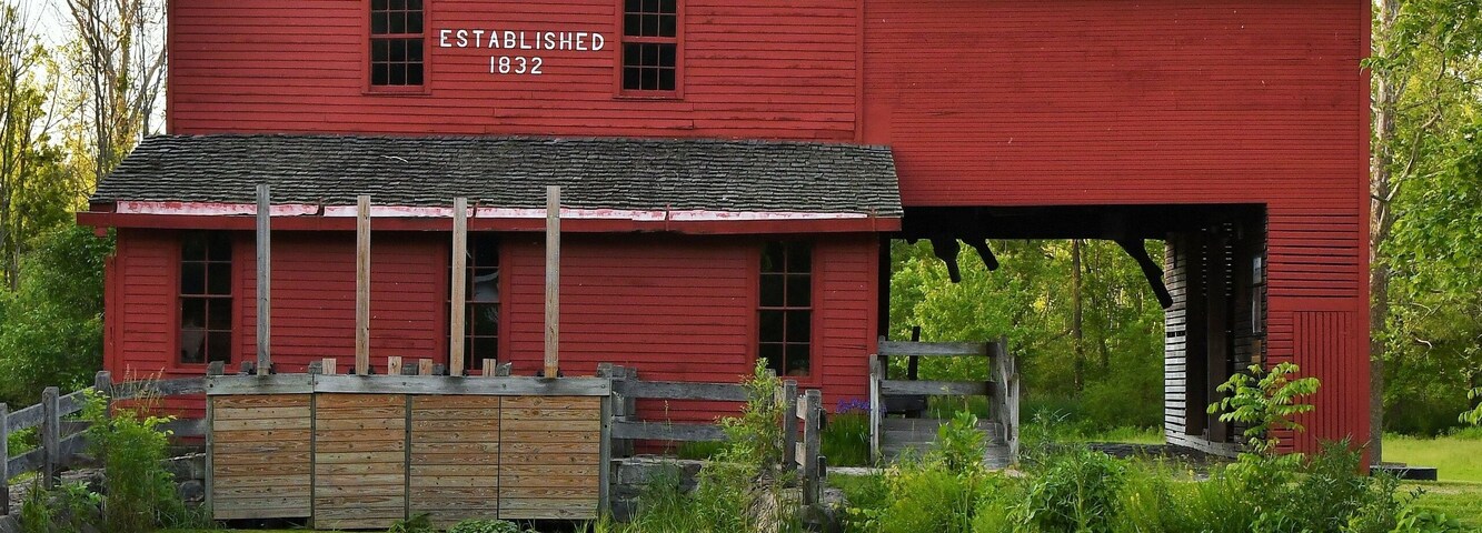 Daytime photo of the red barn mill at Bonneyville Mills in Bristol, Indiana with a calm pond and reflection in the foreground