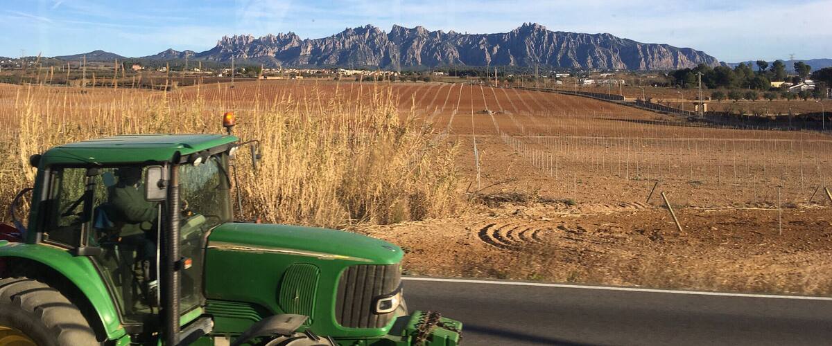 A green tractor on a road with fields and mountains in the background.