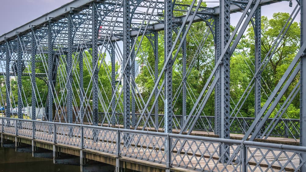 A metal bridge over a river with trees in the background.