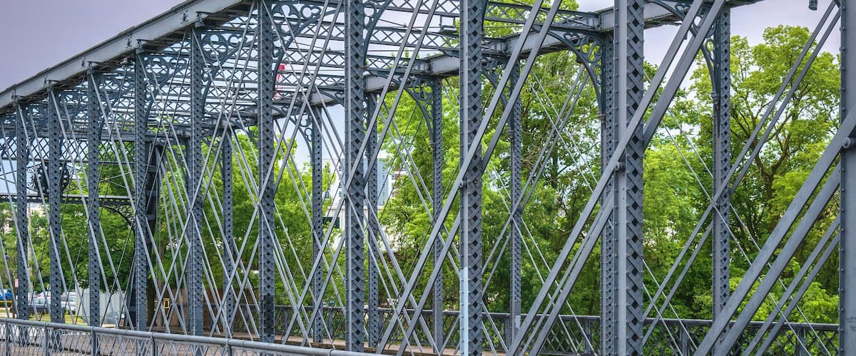 A metal bridge over a river with trees in the background.