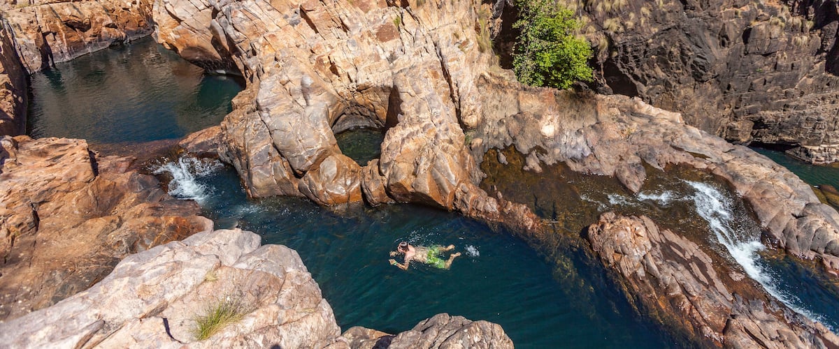 A rocky canyon with a man swimming in a clear blue pool.