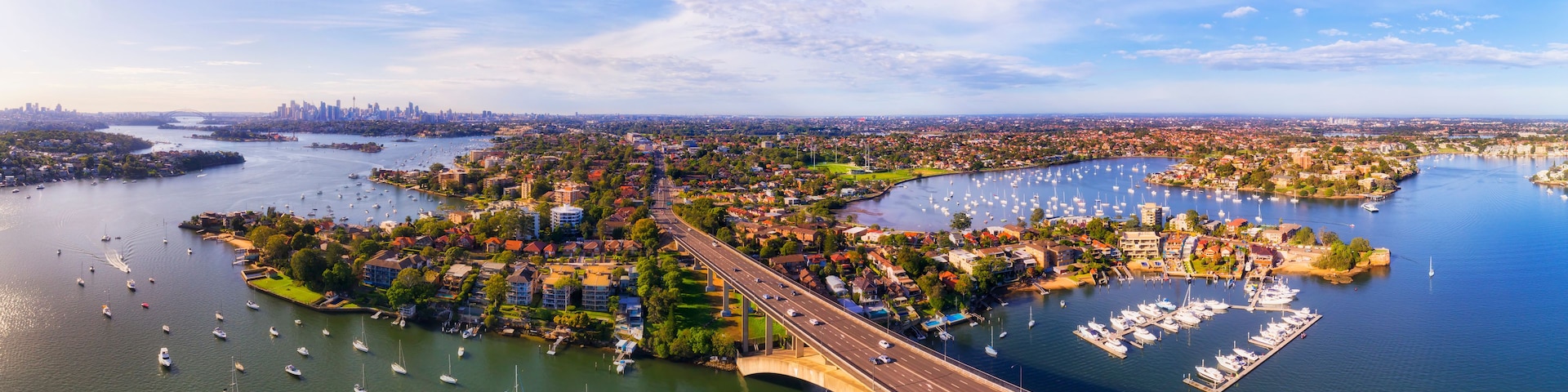 Paisagem costeira com uma ponte, marina e área urbana.