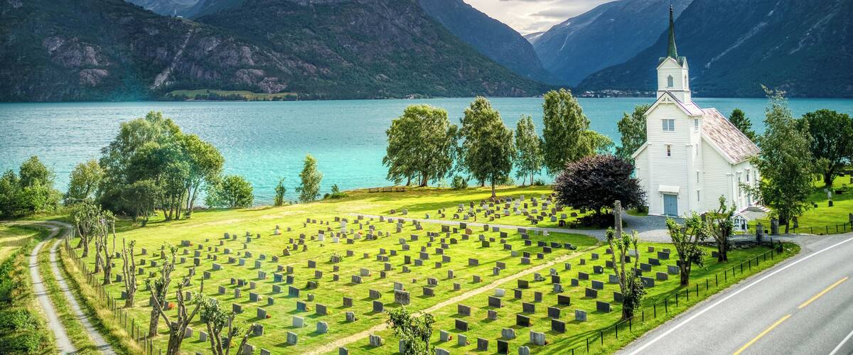 A cemetery with headstones, a church, and mountains in the background.