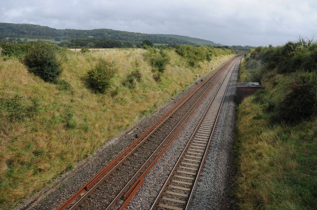Vías de tren en zona rural, con colinas verdes al fondo.