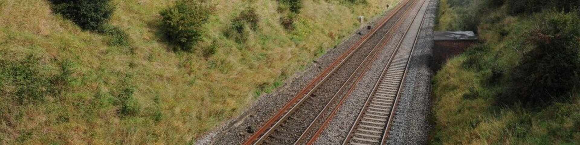 Vías de tren en zona rural, con colinas verdes al fondo.