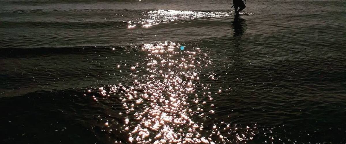 A person standing in shallow water with sunlight reflecting off the surface.