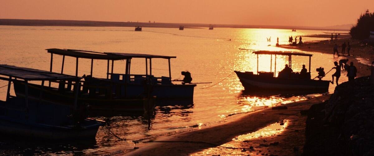 A sunset over a calm river with boats docked along the shore.