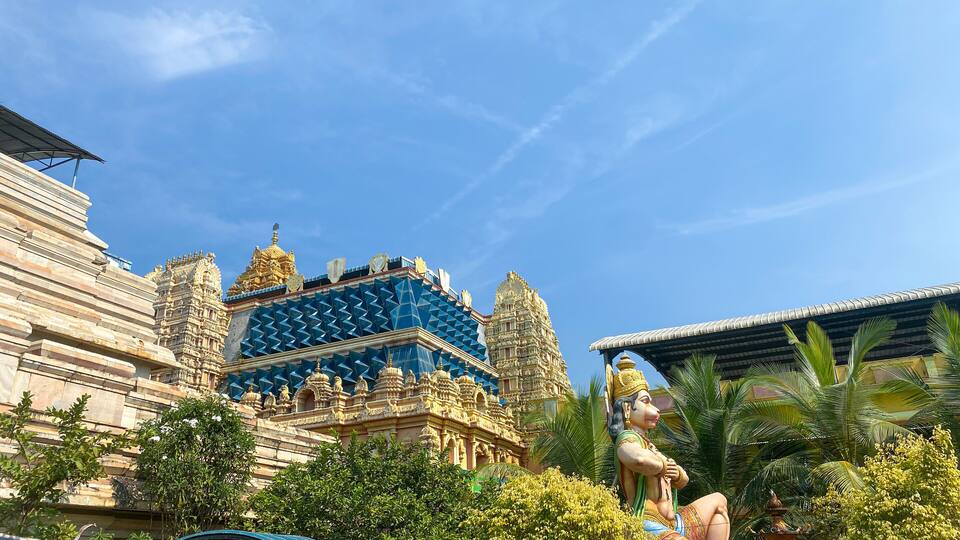 A temple with intricate architecture, a statue of a deity, and lush greenery.