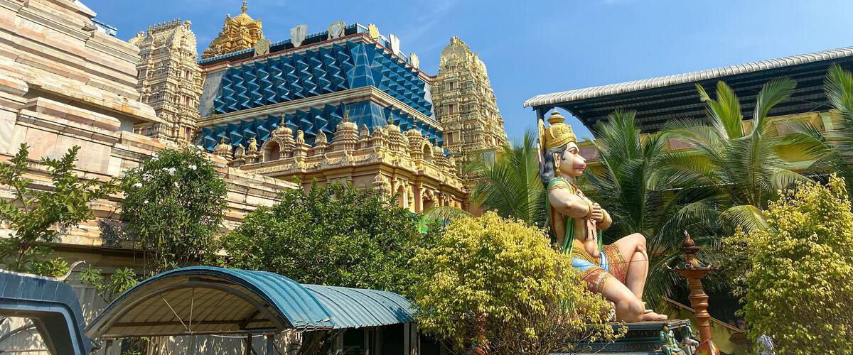 A temple with intricate architecture, a statue of a deity, and lush greenery.