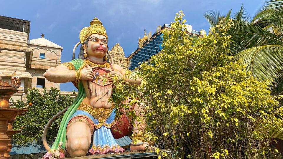 A large statue of a deity with a heart-shaped chest, surrounded by lush greenery and traditional architecture.