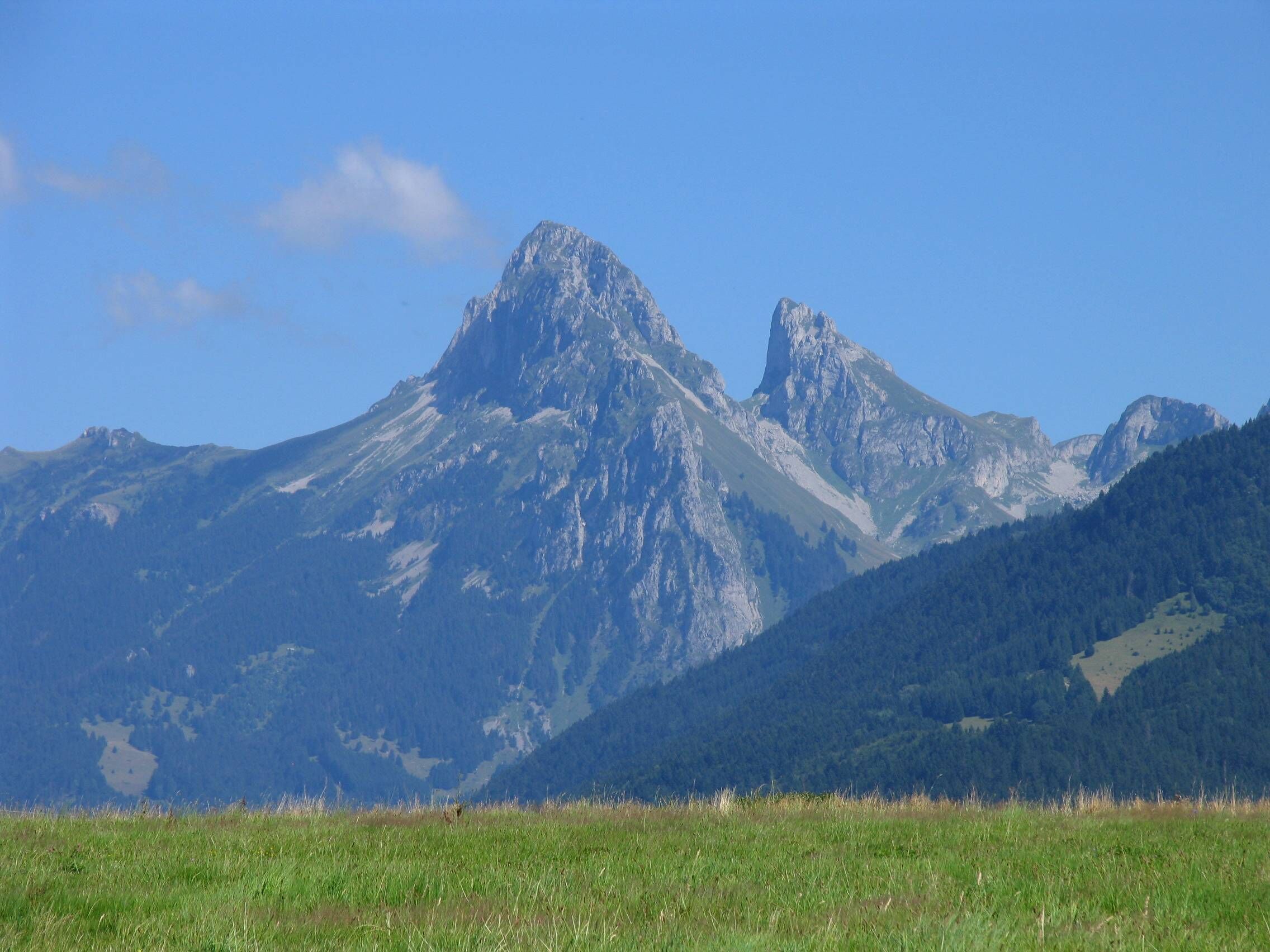 A mountain range with a prominent peak, lush green valleys, and a clear blue sky.