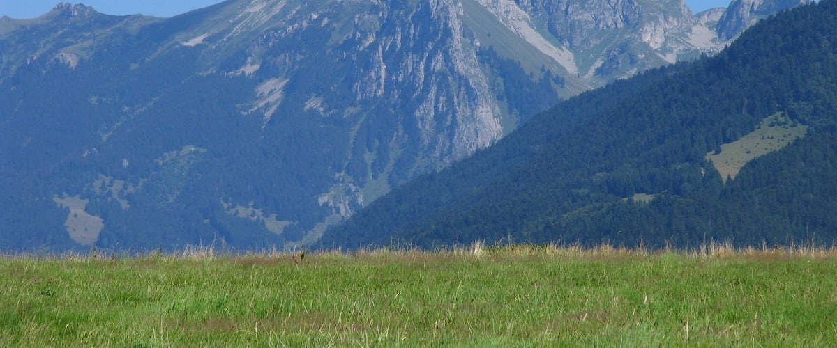 A mountain range with a prominent peak, lush green valleys, and a clear blue sky.