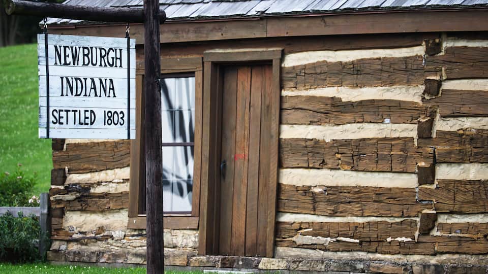 A log cabin with a sign reading "Newburgh, Indiana, Settled 1803."