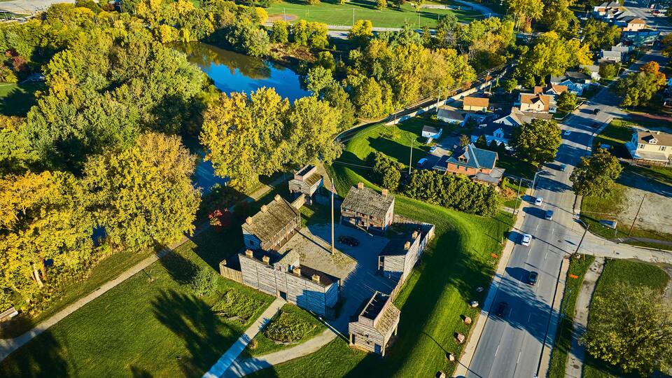 An aerial view of a park with a pond, surrounded by trees and residential buildings.