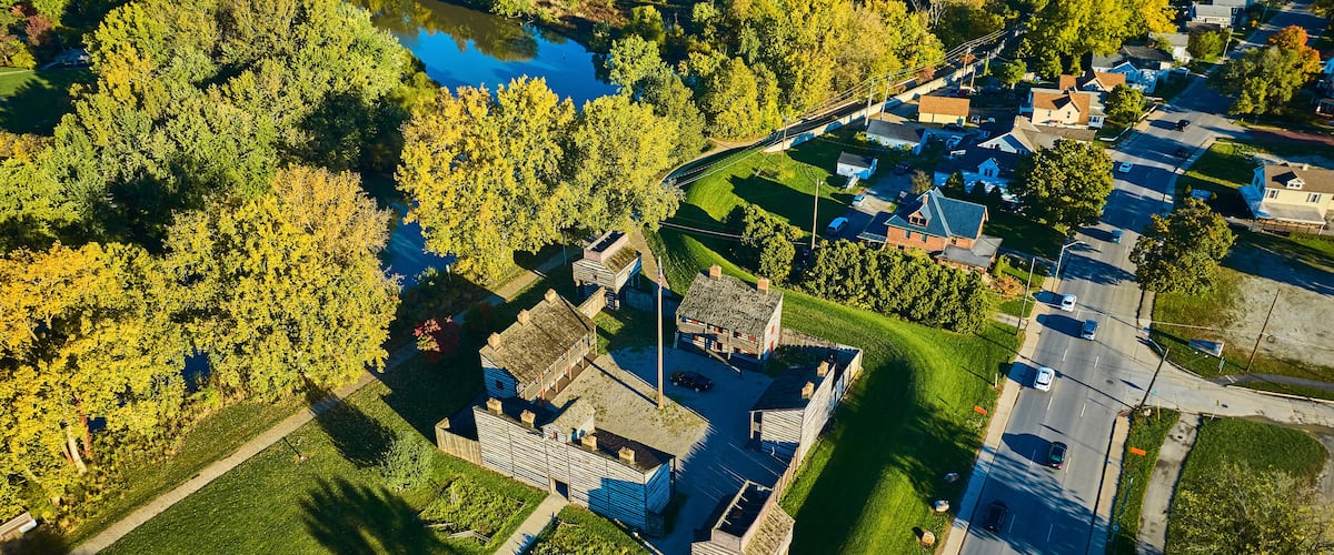 An aerial view of a park with a pond, surrounded by trees and residential buildings.