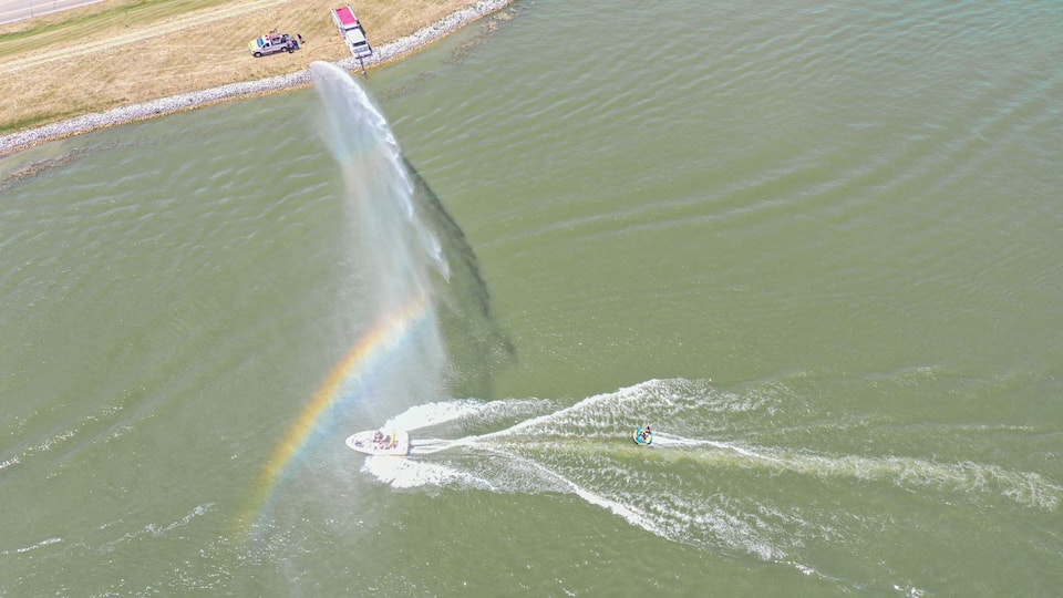 A body of water with a rainbow, a jet ski, and a boat.