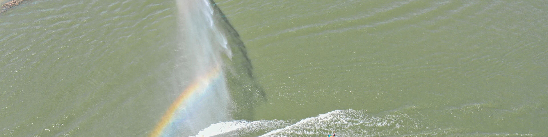 Ein Gewässer mit Regenbogen, Jetski und Boot.