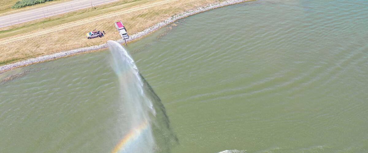 A body of water with a rainbow, a jet ski, and a boat.