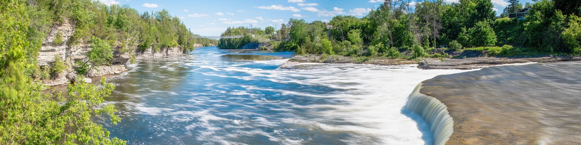 A river with a waterfall, surrounded by dense greenery and a clear sky.