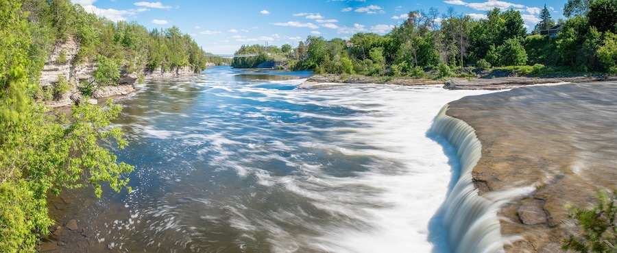 A river with a waterfall, surrounded by dense greenery and a clear sky.