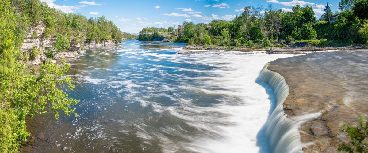 A river with a waterfall, surrounded by dense greenery and a clear sky.