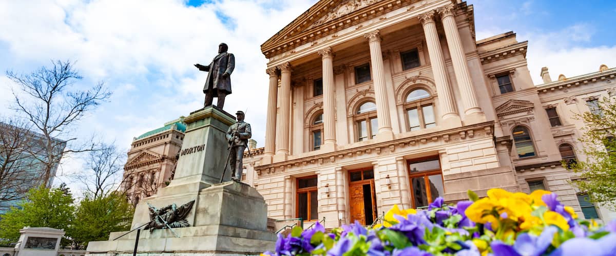 A classical building with a statue in front, surrounded by vibrant flowers.